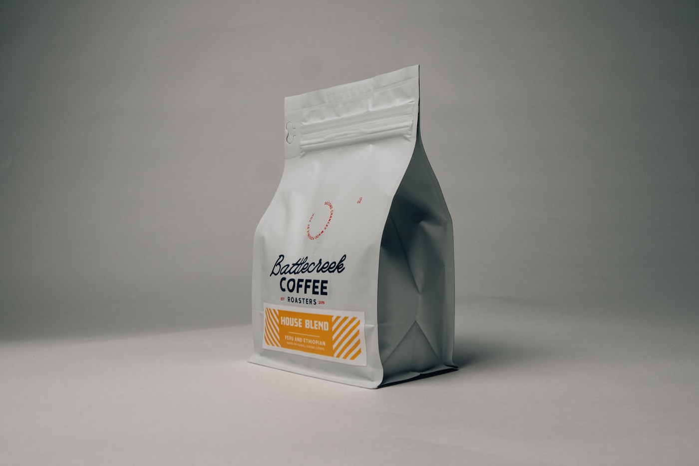 A kraft-paper coffee bag tipped on its side with whole beans scattered around it.