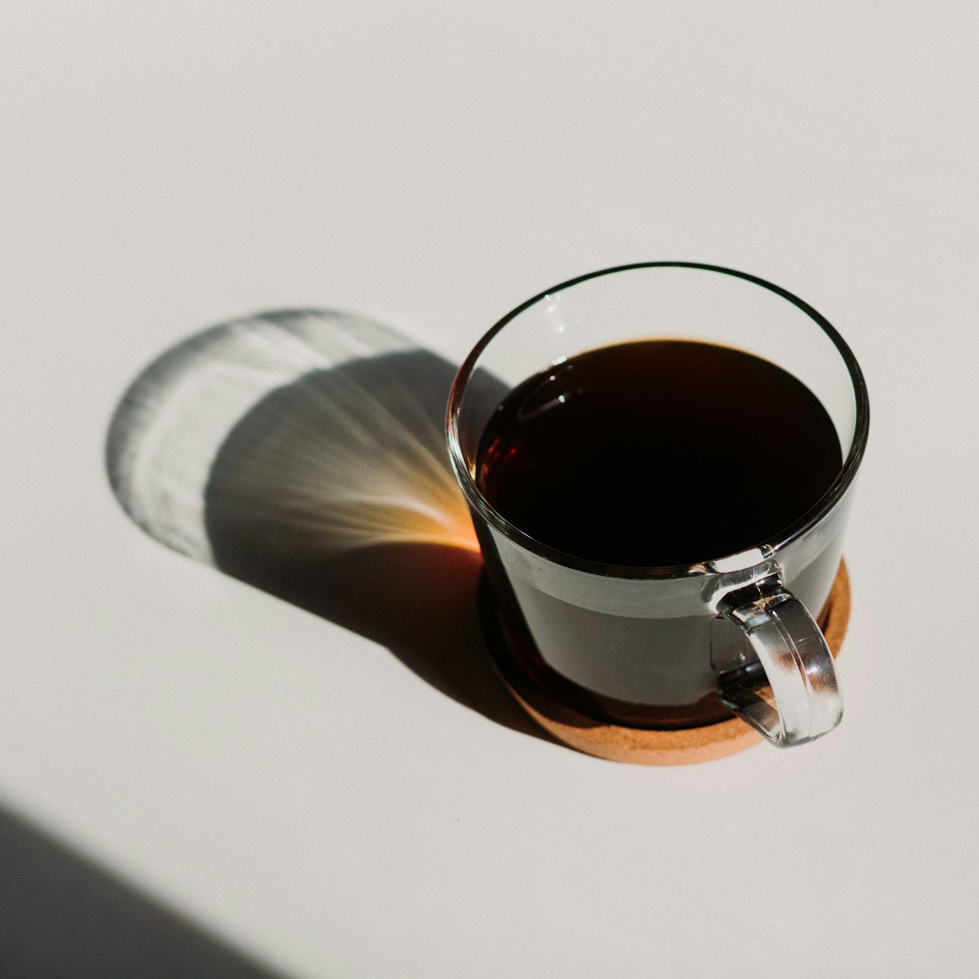 A glass pour-over dripper releasing coffee into a carafe, steam rising in side light.